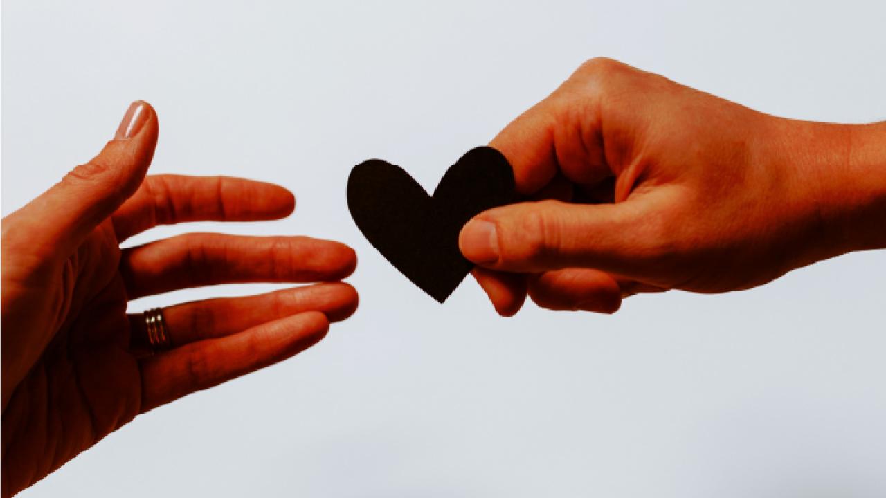 One hand giving a paper heart to another hand.